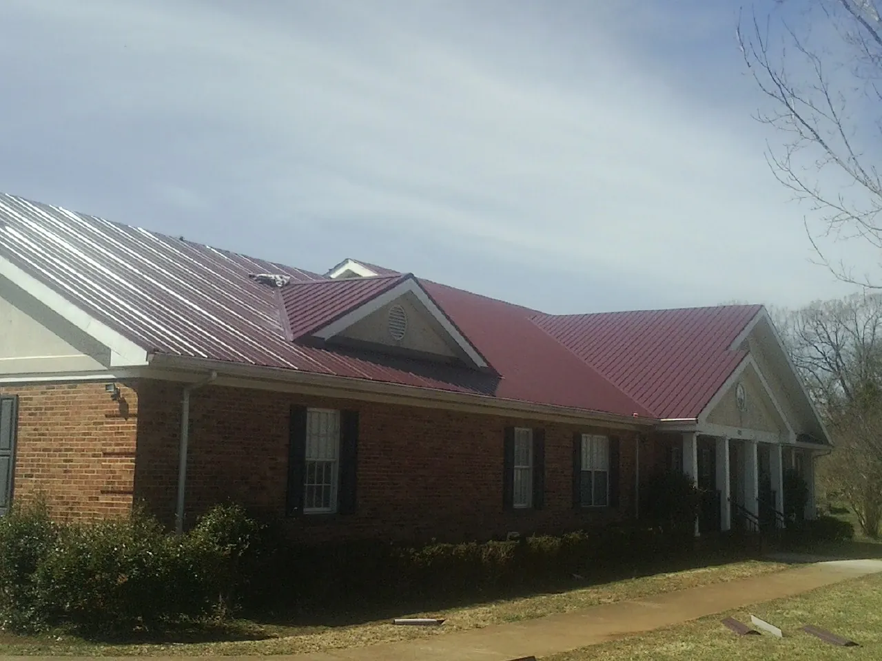 Red metal roof with gabled entries on a long brick building, from a Hail Damage Roof Repair job in Arlee