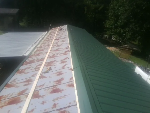 Old rusted panels beside newly installed green metal roofing — Wind Damage Roof Repair by Roofing Brothers in Arlee