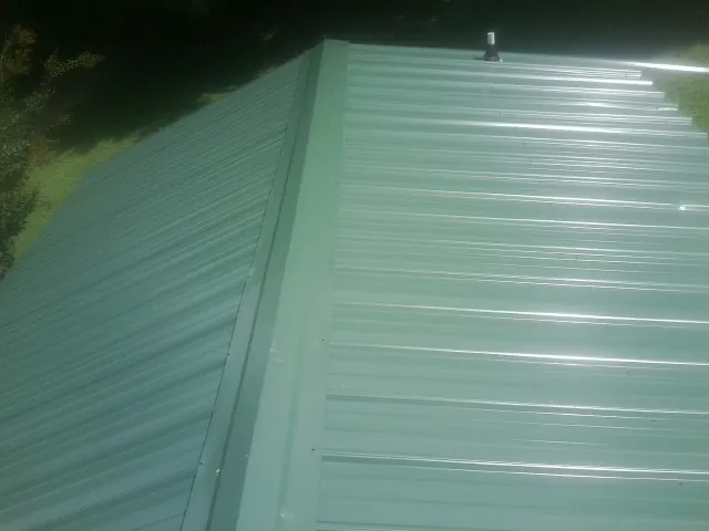 New green metal panels meeting at the ridge of a roof — Flat Roof Repair work by our crew in Arlee
