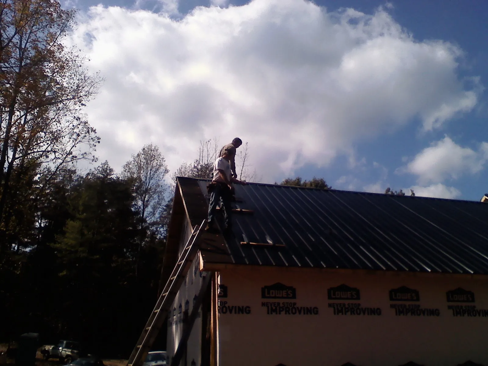 Roofer fastening dark metal panels high against a cloudy sky, from a Roof Inspection job in Arlee